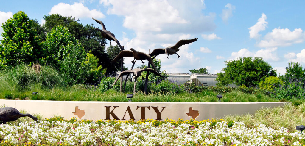  Sign that says Katy and has the shape of Texas state on it. It has statues of birds flying.