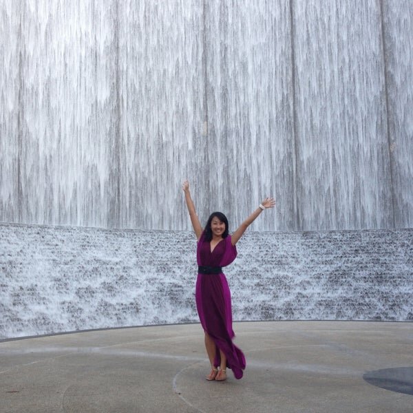 Lady sold her house to a cash buyer after a divorce. She is standing in front of the Hines Waterwall in Houston, Texas with her arms in the air. Excited to move on to the next chapter in life.