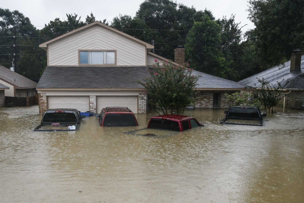 Picture of a house in Houston that is flooded. The water level is half way up the garage door and the four cars in the front are half way covered with water.