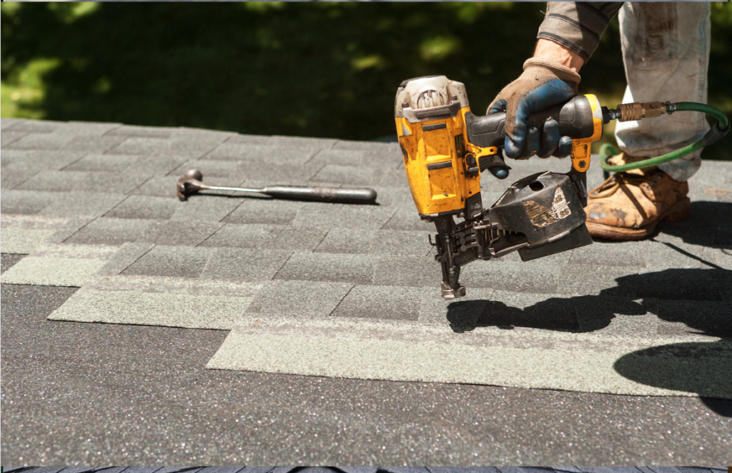 Roofer with a nail gun putting on new shingles for a roof.