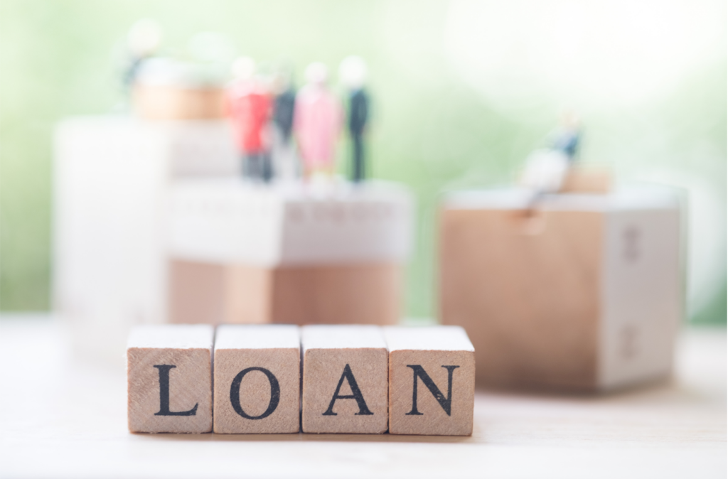 picture of blocks with LOAN written on them. Figures of people are blurred in the background