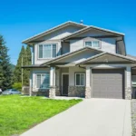 Modern two-story house with a gray exterior, attached garage, green lawn, and concrete driveway.