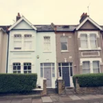 Row of colorful terraced houses with front doors, large windows, and neatly trimmed hedges.