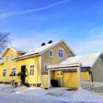 Yellow and beige two-story house with white trim, snow-covered roof, and front yard in winter.