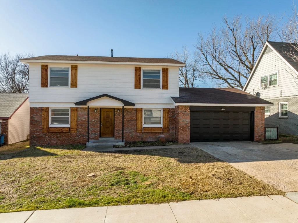 Two-story brick and white home with black two-car garage door and wood shutter accents in Jenks
