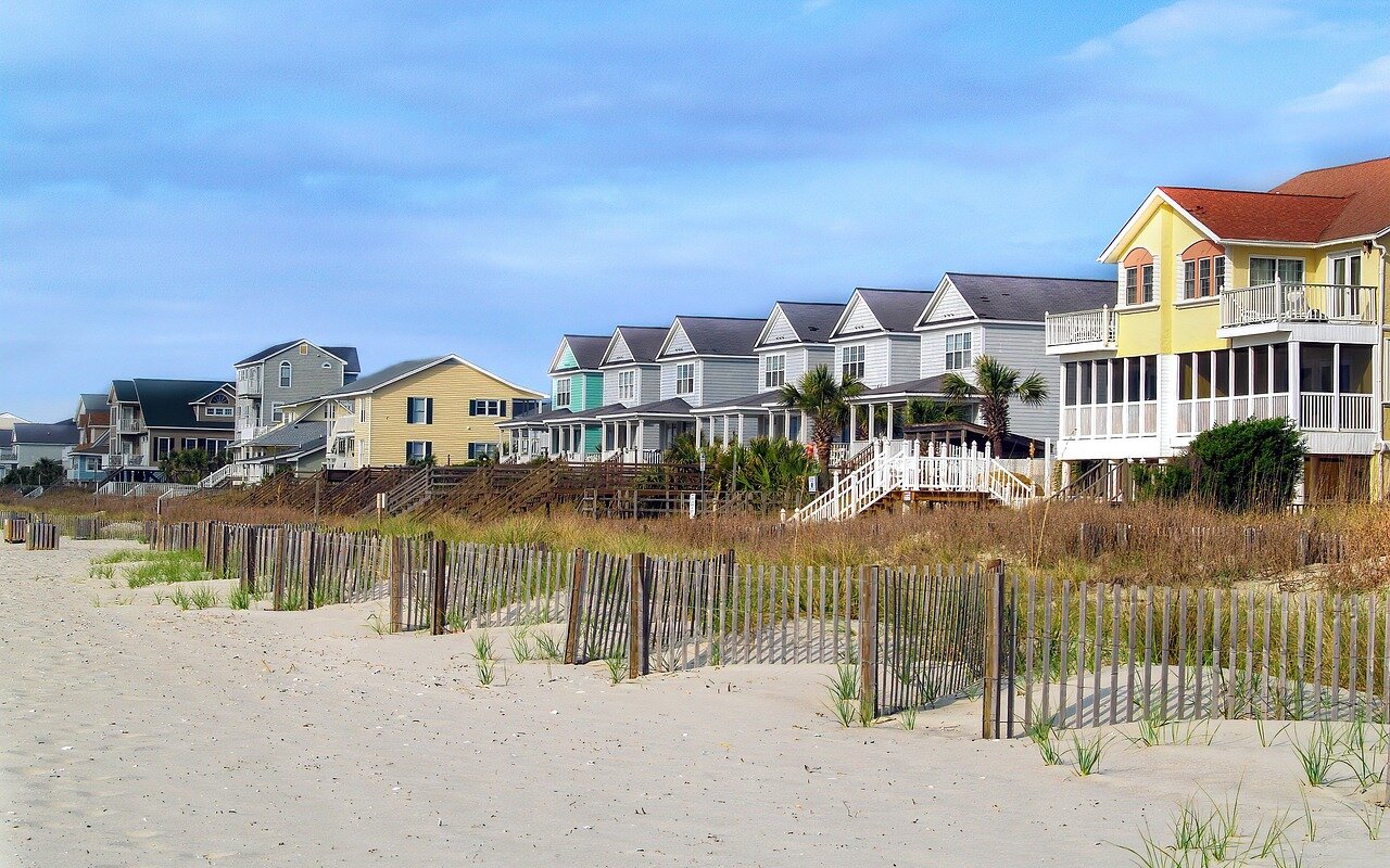 Colorful beach homes in North Carolina lined up in a row and one house is for sale for cash to local home buyers.