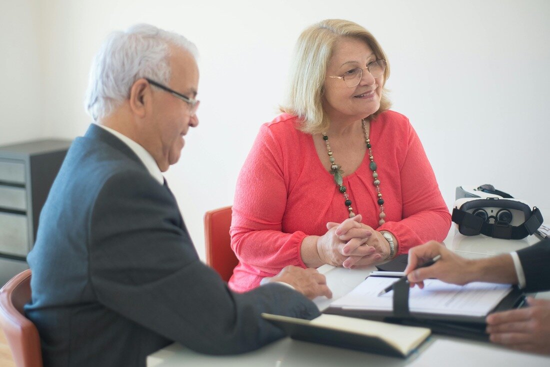 Married couple are homeowners in NC and sitting at desk of real estate attorney to learn how to sell home for cash