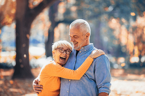 Old white husband and wife smiling and hugging each other while walking in park