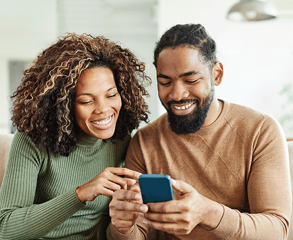 young african american husband and wife smiling while they look at their phone