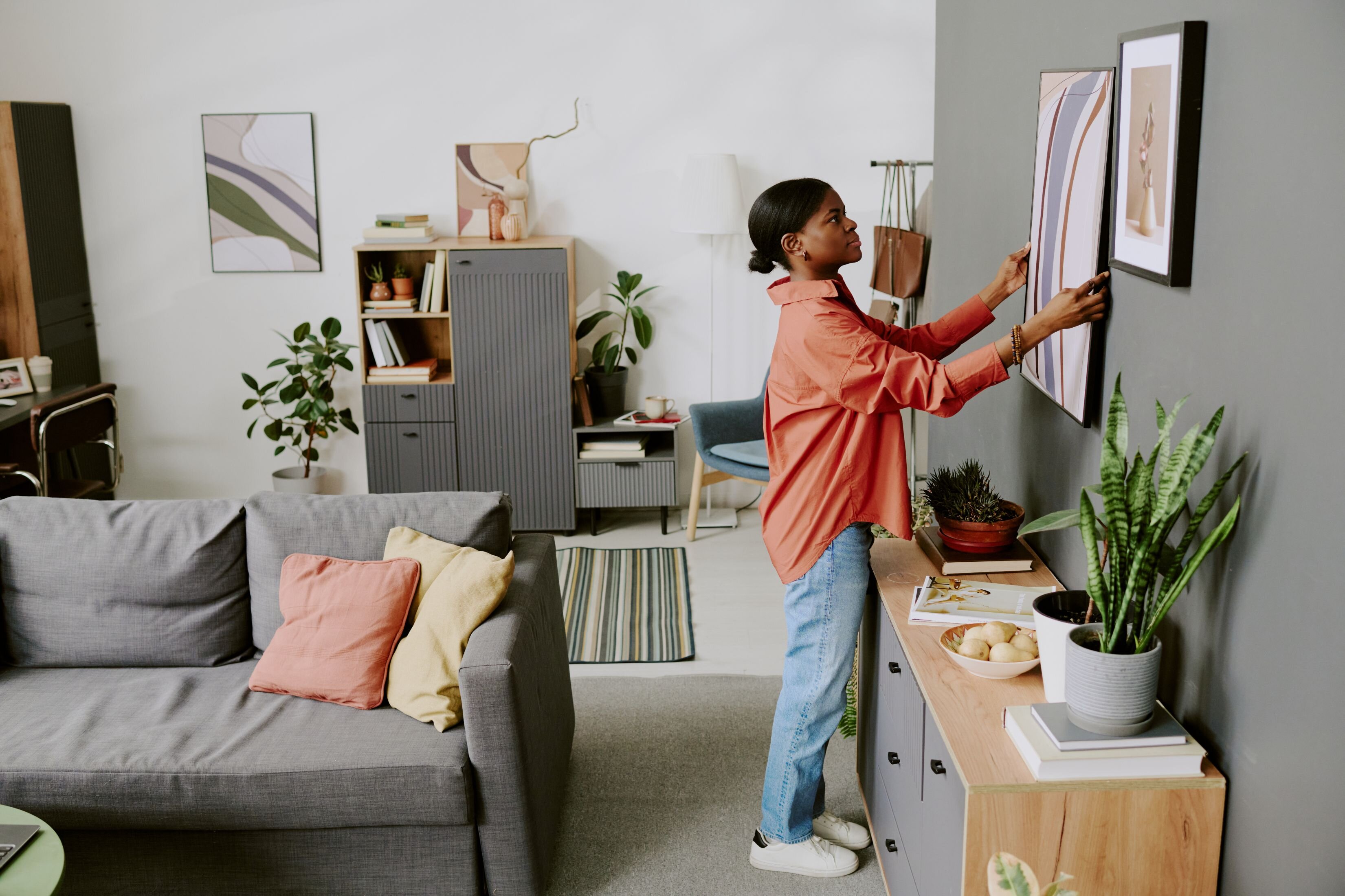 This image displays someone placing a piece of art on the wall, showing one of the ways a homeowner can stage their home before selling.