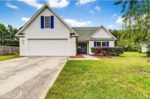 Single-story home with a two-car garage and blue shutters on a large green lot in Jacksonville, NC