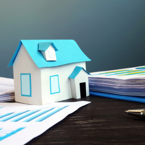 Small paper house, pile of documents and a pen on a table