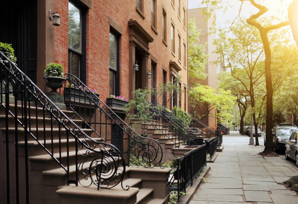 A street in New York city with red brick brownstone homes and steps with beautiful iron banister railing.