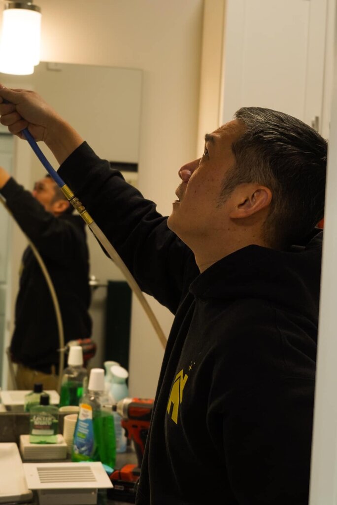 A man in a black hoodie working on a bathroom mirror for air duct cleaning clagary service near me