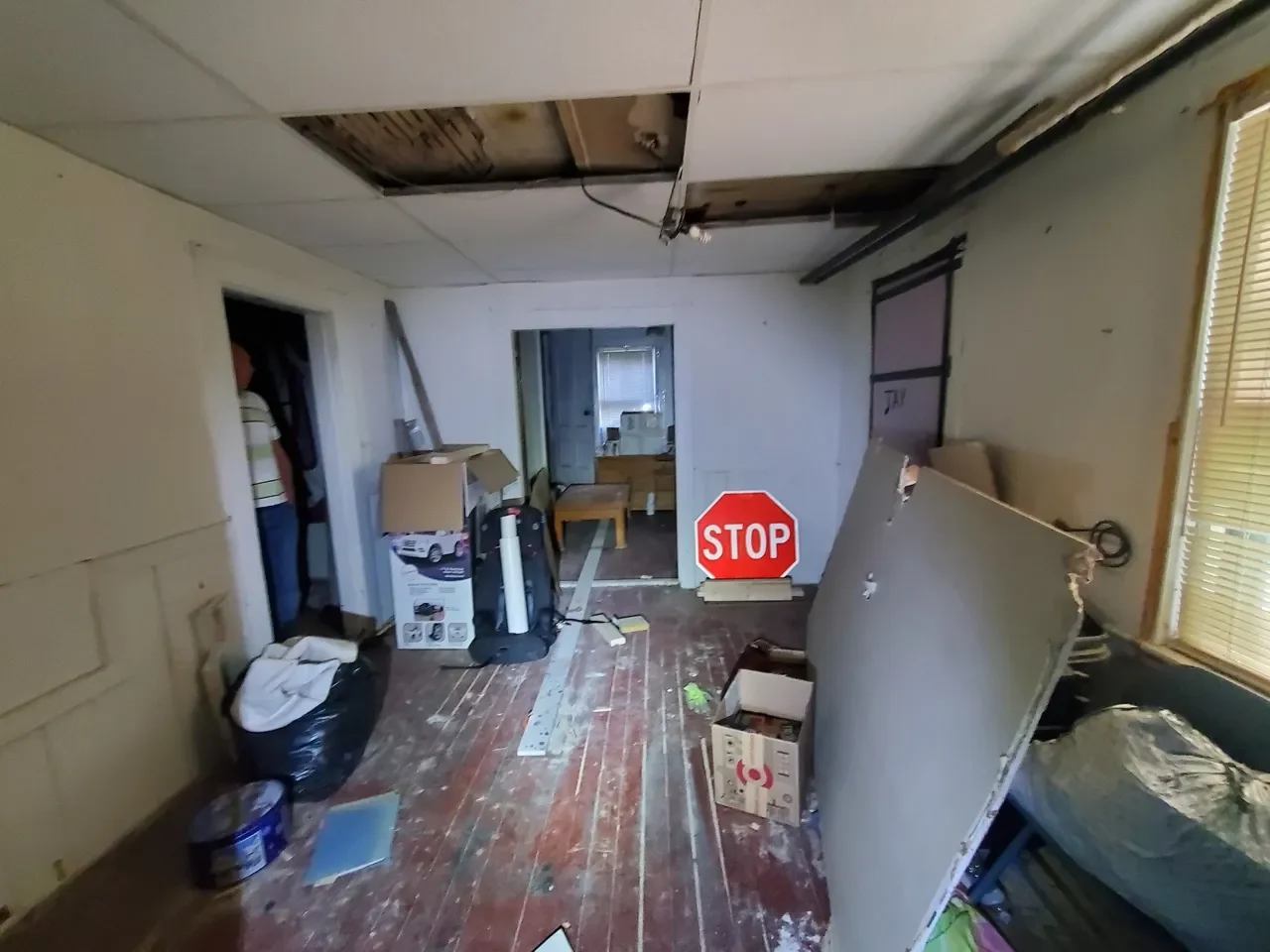 Messy room with a damaged ceiling, unfinished walls, and worn wooden flooring that require extensive repair and renovation.