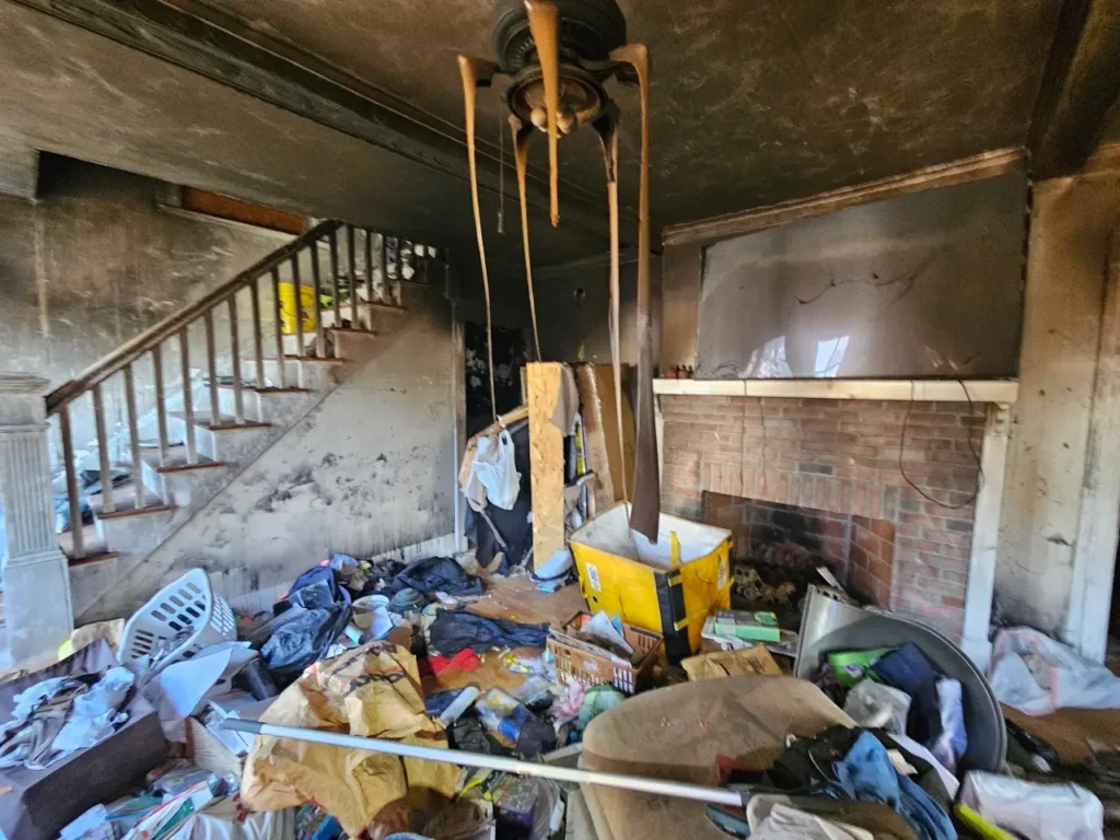 Living room in a Greater Boston home needing major repairs with fire damage, debris, and exposed brick fireplace