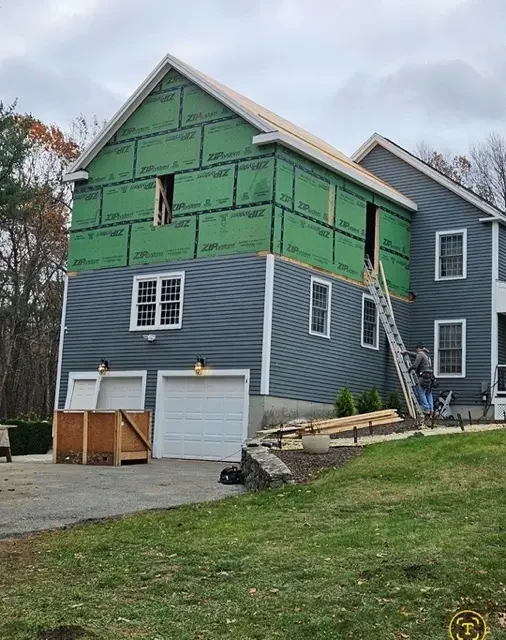 Side view of a home undergoing construction with new framing and green sheathing additions