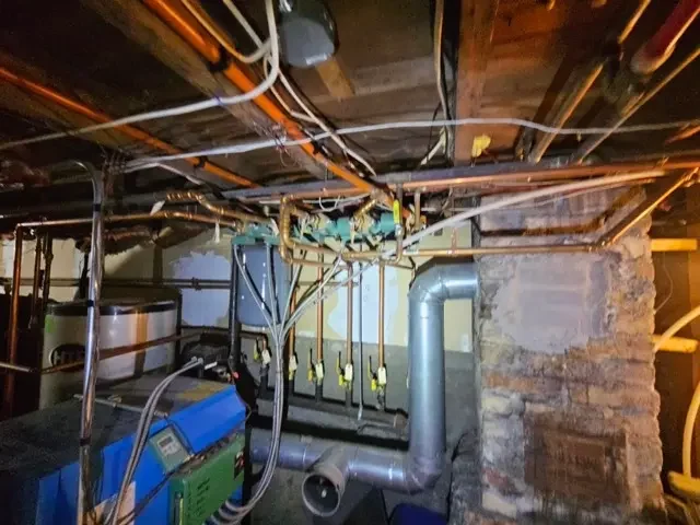 Basement utility area showing complex plumbing pipes, water heater, and heating system needing repairs