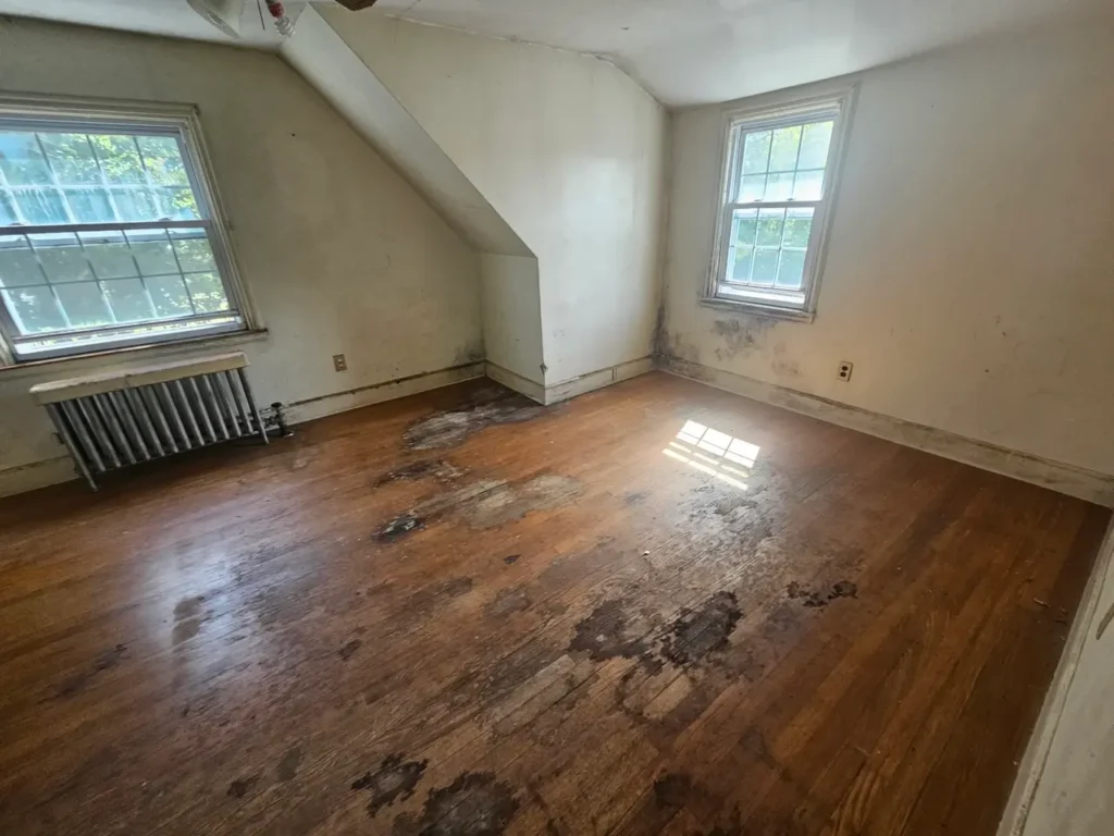 Empty bedroom in a Massachusetts house showing severe water damage and stains on the wooden floor
