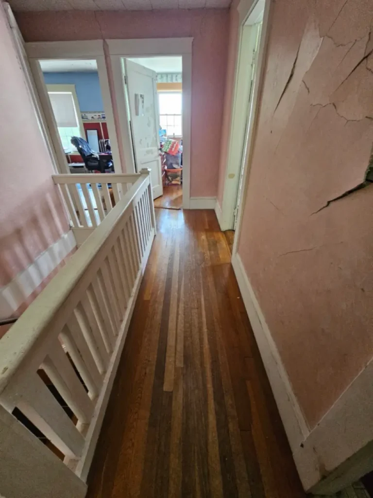 Second-floor hallway in a Massachusetts house with cracked pink plaster walls and hardwood floors