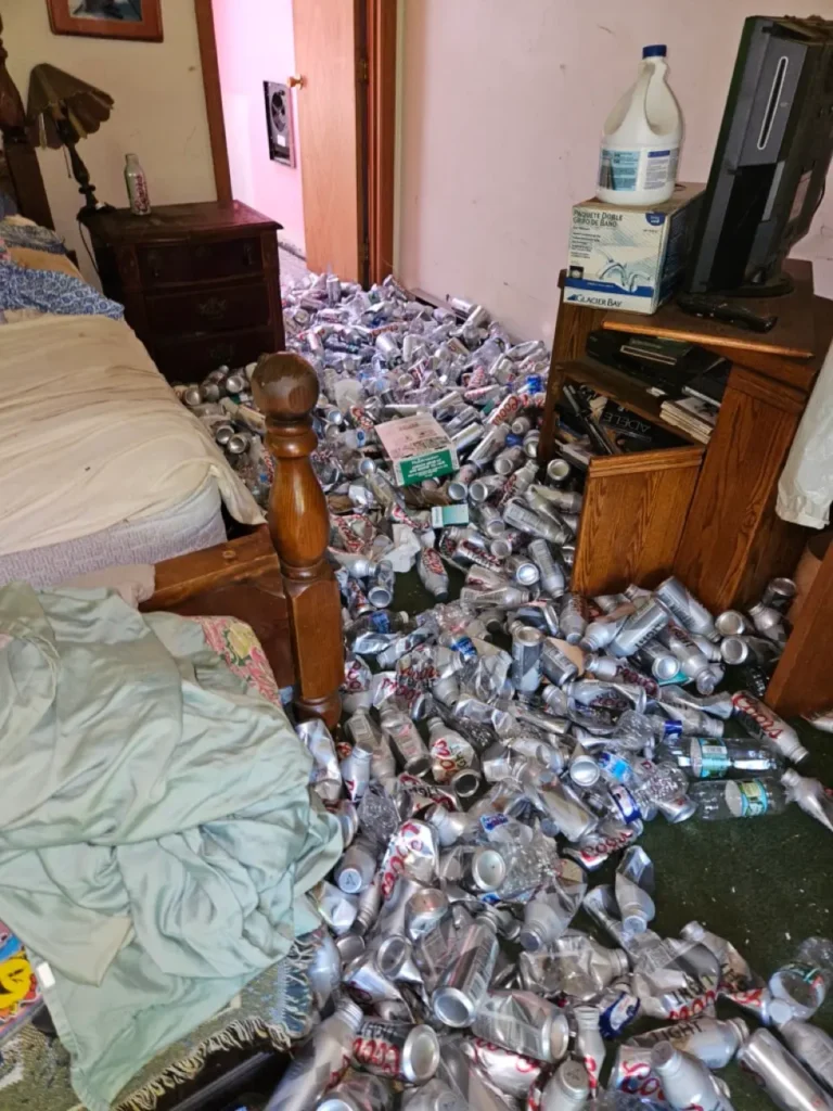 Bedroom floor heavily littered with discarded beer cans and trash in a MetroWest home with severe hoarding issues