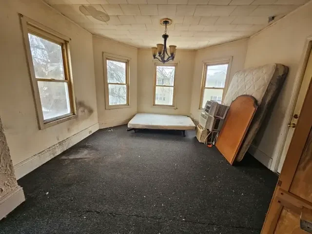 Empty bedroom in a Worcester fixer-upper home featuring old carpeting, stained walls, and a mattress