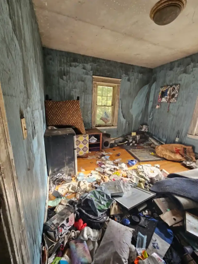 Damaged interior room of a Worcester house featuring peeling blue walls and heavy debris on the floor