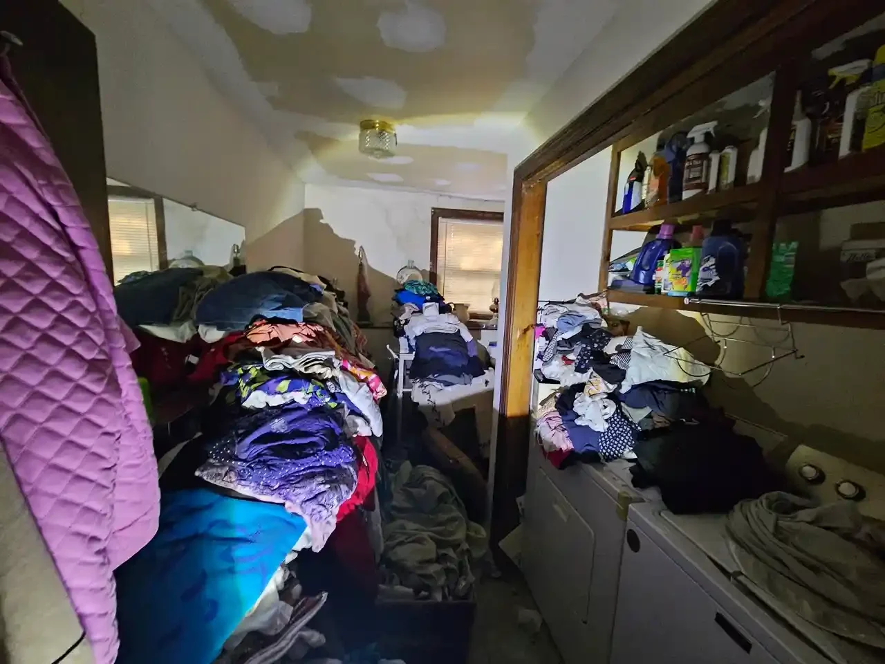 Cluttered laundry room and hallway in a Worcester house filled with piled clothing and storage issues
