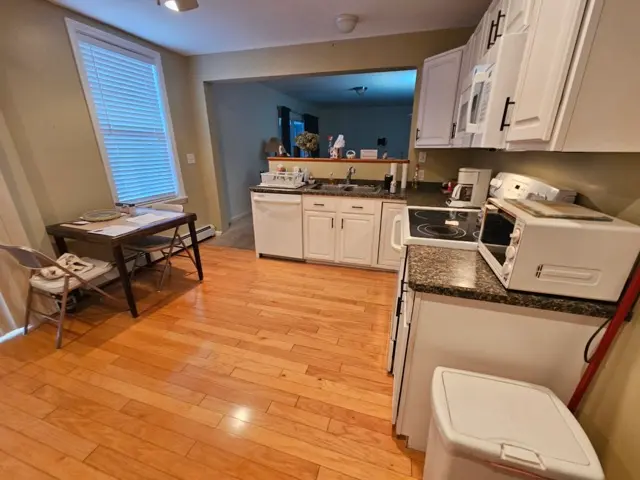 Kitchen with white cabinets, wood flooring, and a small table for dining.