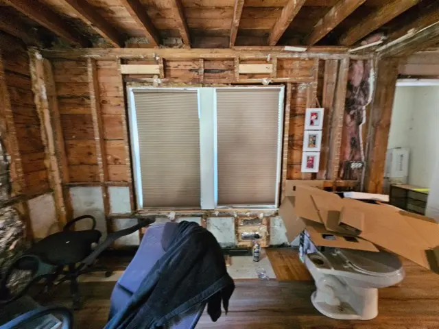 Room with exposed wall studs, flooring, and windows that need repair.
