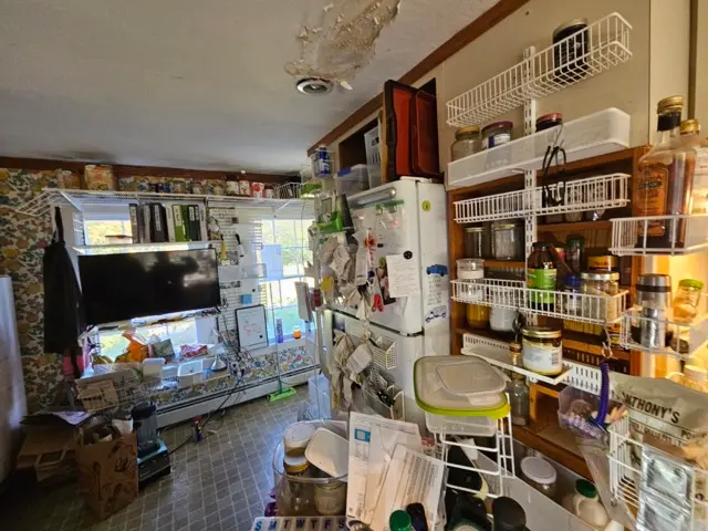 A cluttered kitchen featuring a ceiling with severe water damage, peeling paint, and staining that require repair.