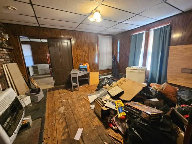 Living room cluttered with cardboard boxes and dirt, featuring flooring that requires extensive repair
