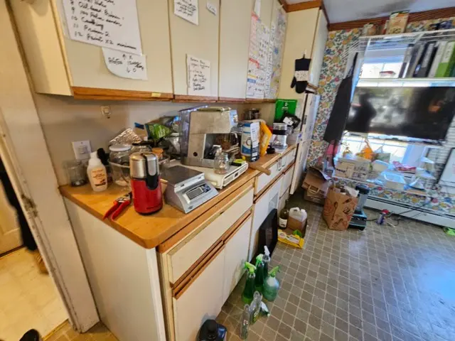 Cluttered kitchen with worn countertops and lower cabinet doors that require repair.