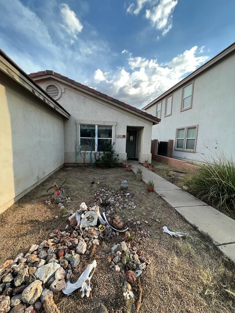 Overgrown weeds and junk in front of a Tucson home causing a property maintenance code violation.