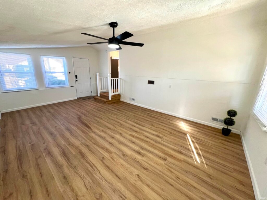 Large bonus room showing access to kitchen and a small plant. It has a new ceiling fan.