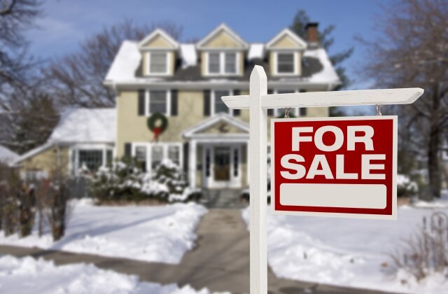 House with a 'For Sale' sign in the front yard, surrounded by snow on a winter day.