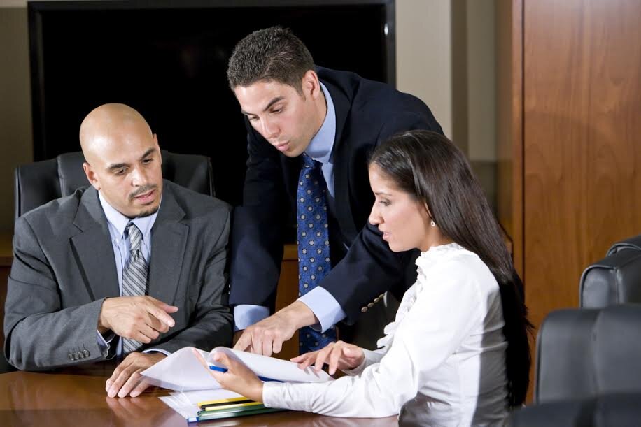 Three professionals in a meeting reviewing documents, with one pointing to a page for discussion.
