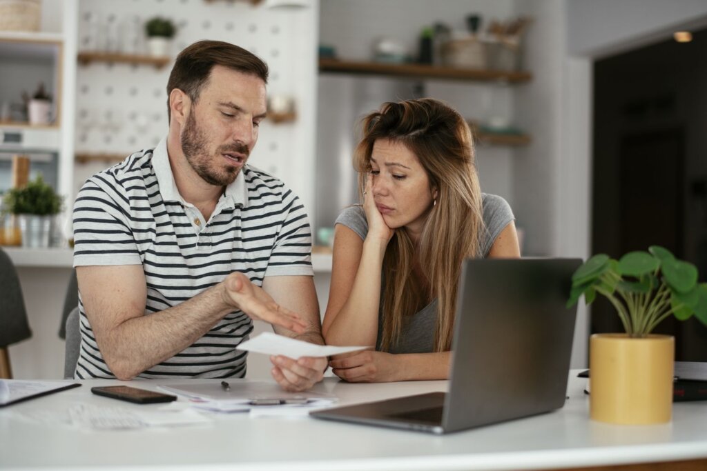 Concerned couple reviewing financial documents at a table with a laptop.