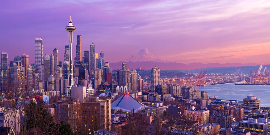 Seattle skyline at sunset with the Space Needle and Mount Rainier in the background, overlooking the city and waterfront.