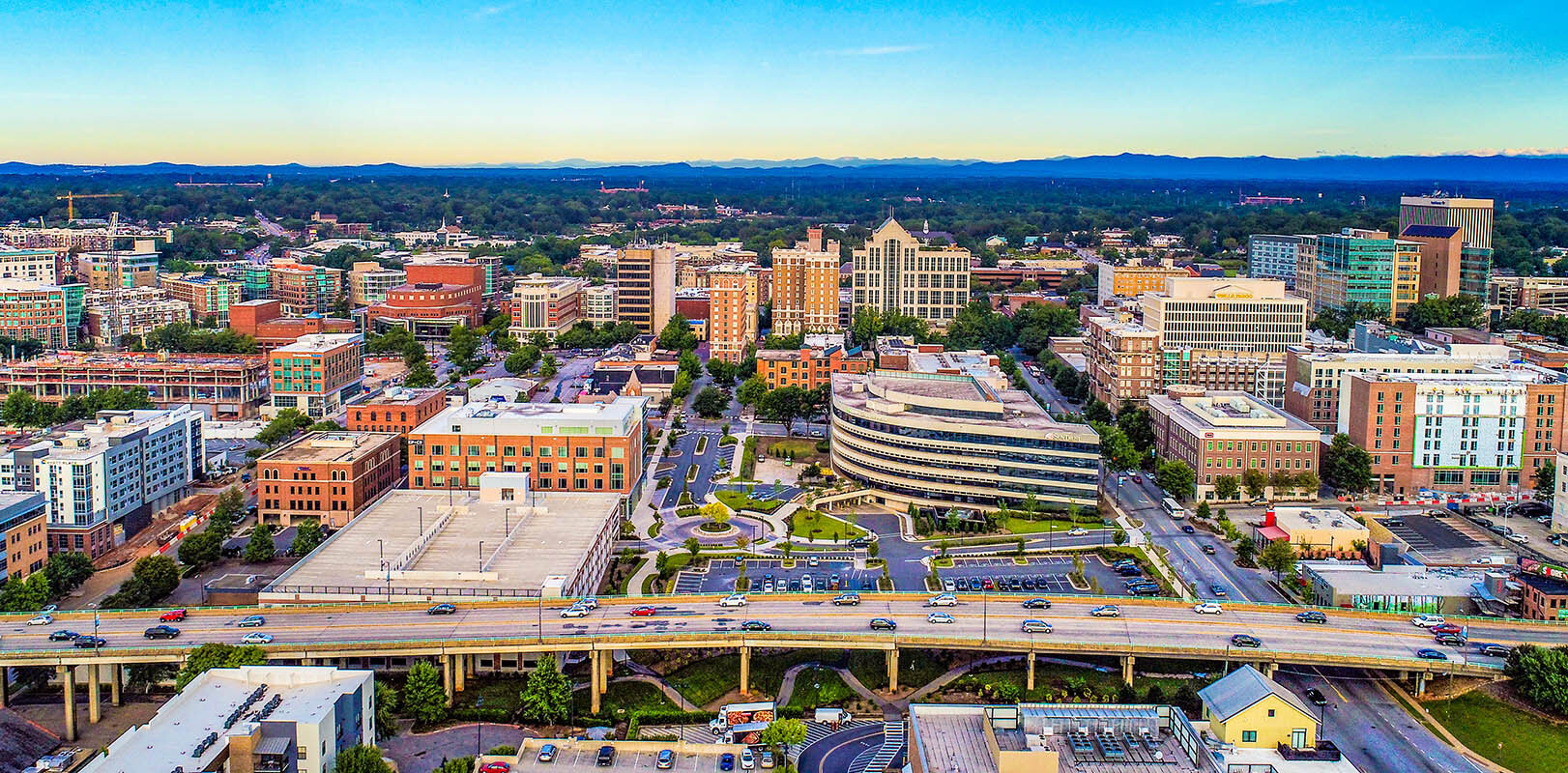 A vibrant aerial view of downtown Greenville, South Carolina, showcasing a mix of modern and historic architecture under a bright blue sky.