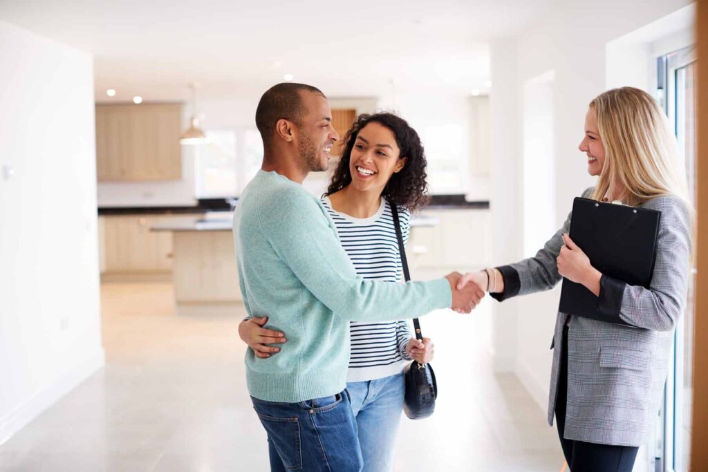 Happy couple shaking hands with a real estate agent in a modern home.