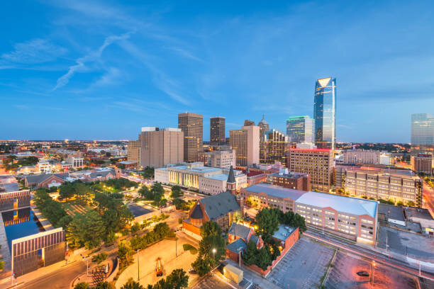 Skyline view of a city at dusk with illuminated buildings and a clear evening sky.