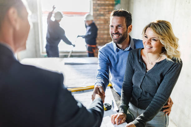 Smiling couple shaking hands with a contractor at a construction site.