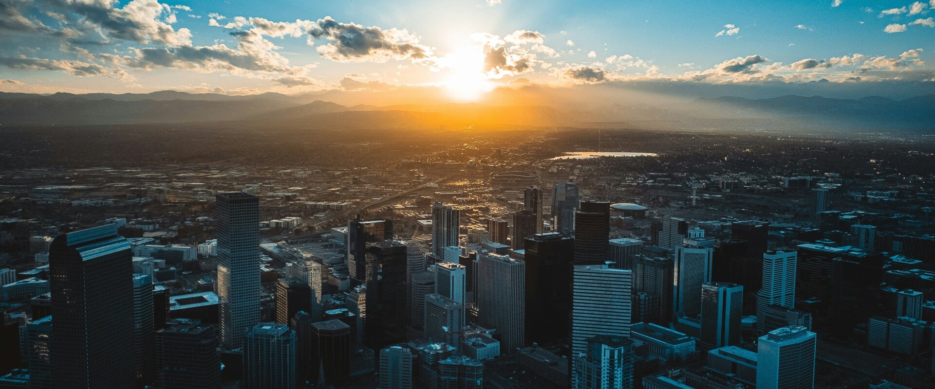A city skyline with skyscrapers during a dramatic sunset, with mountains in the background.