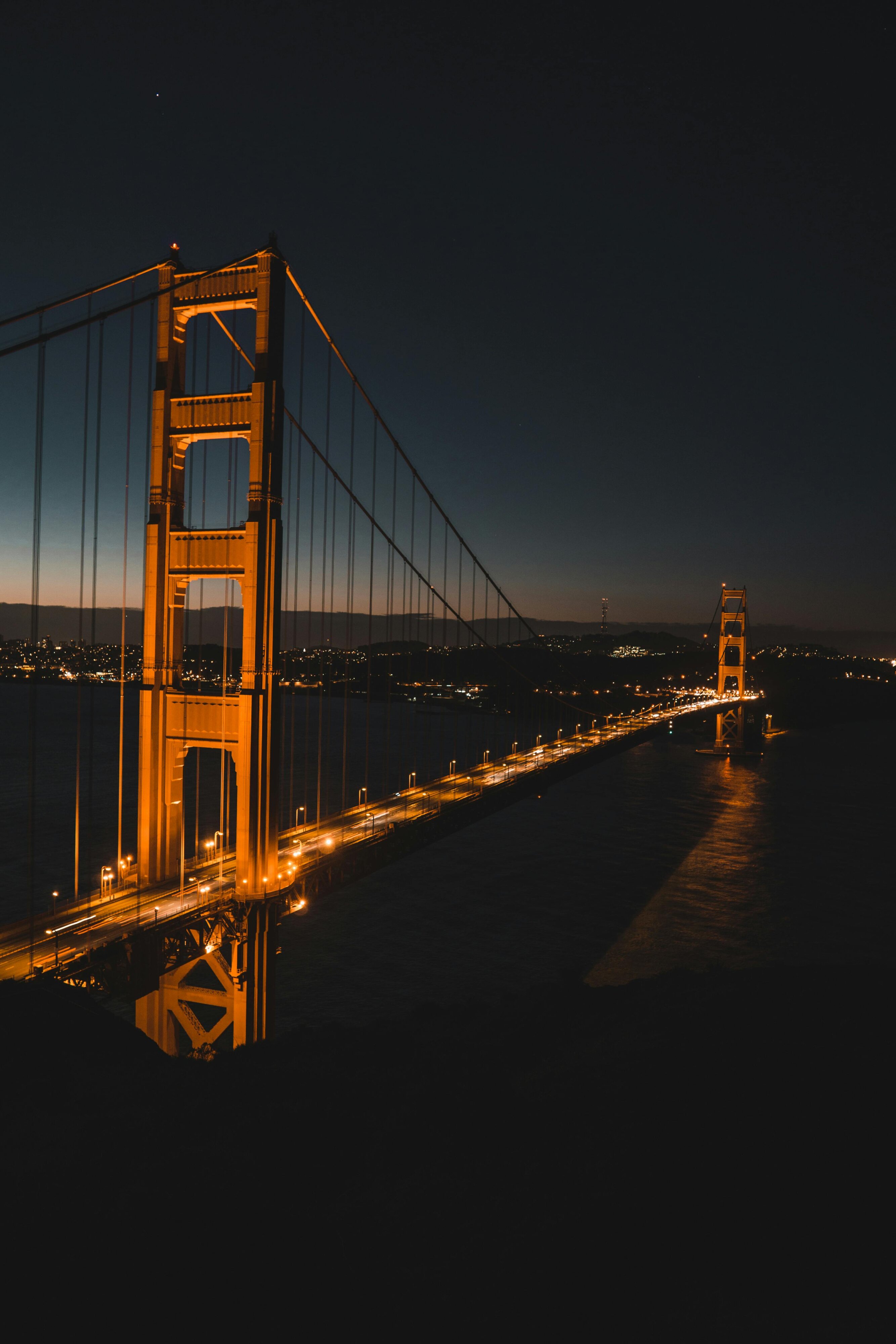 Golden Gate Bridge at night, illuminated against the dark sky, with the city lights in the distance.