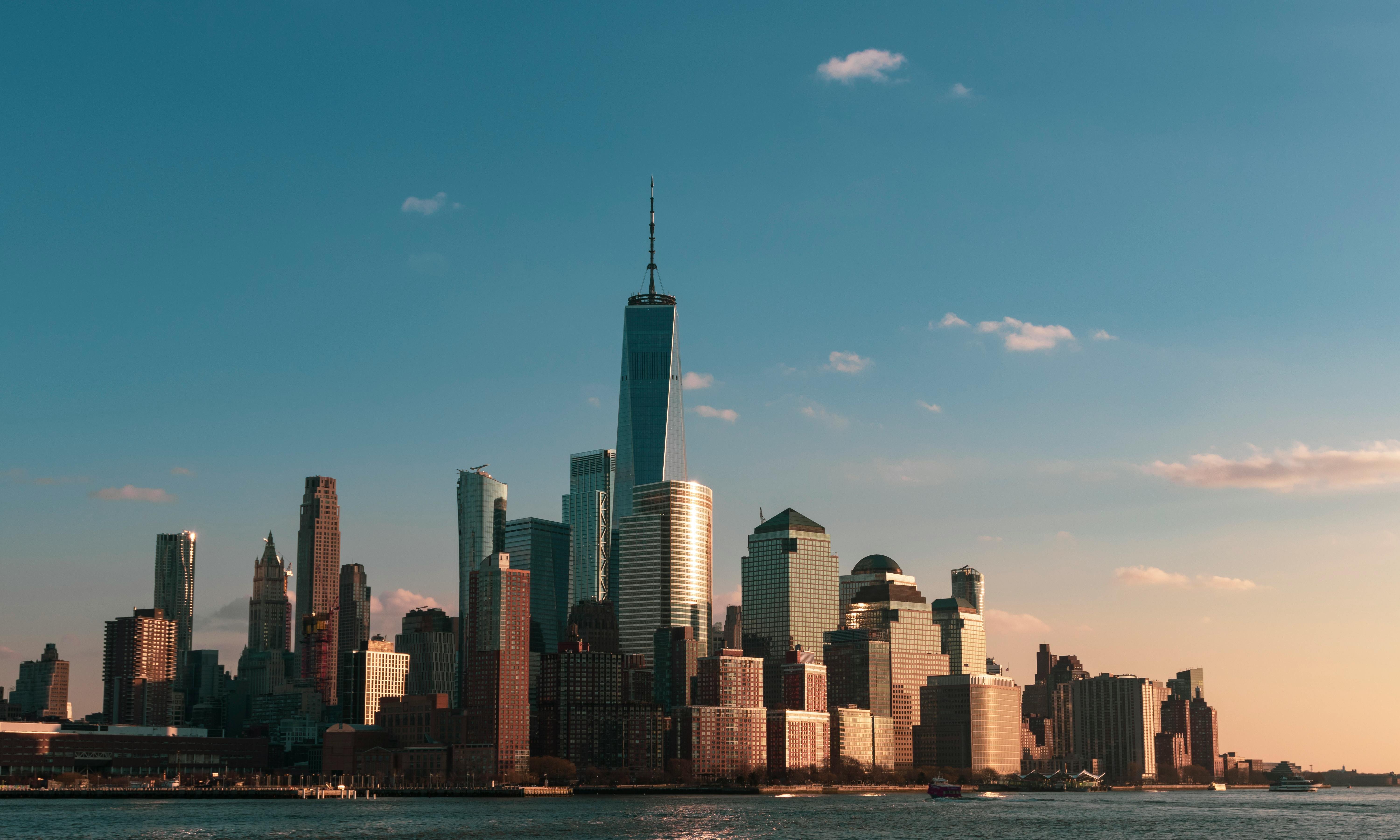 Manhattan skyline during sunset, highlighting the One World Trade Center with reflections on the Hudson River.