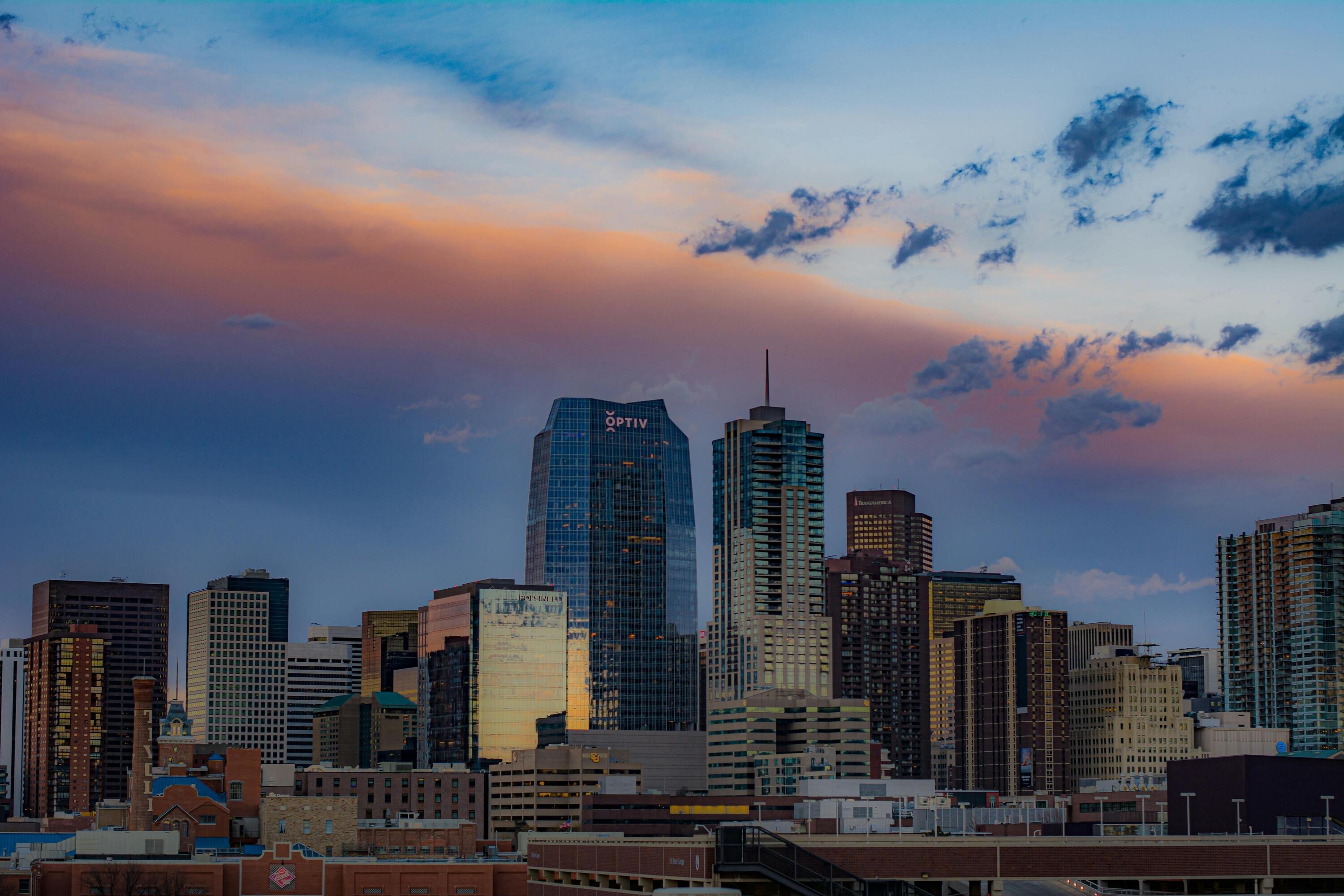 A city skyline with modern skyscrapers reflecting the evening light, set against a dramatic sky with orange and blue hues.