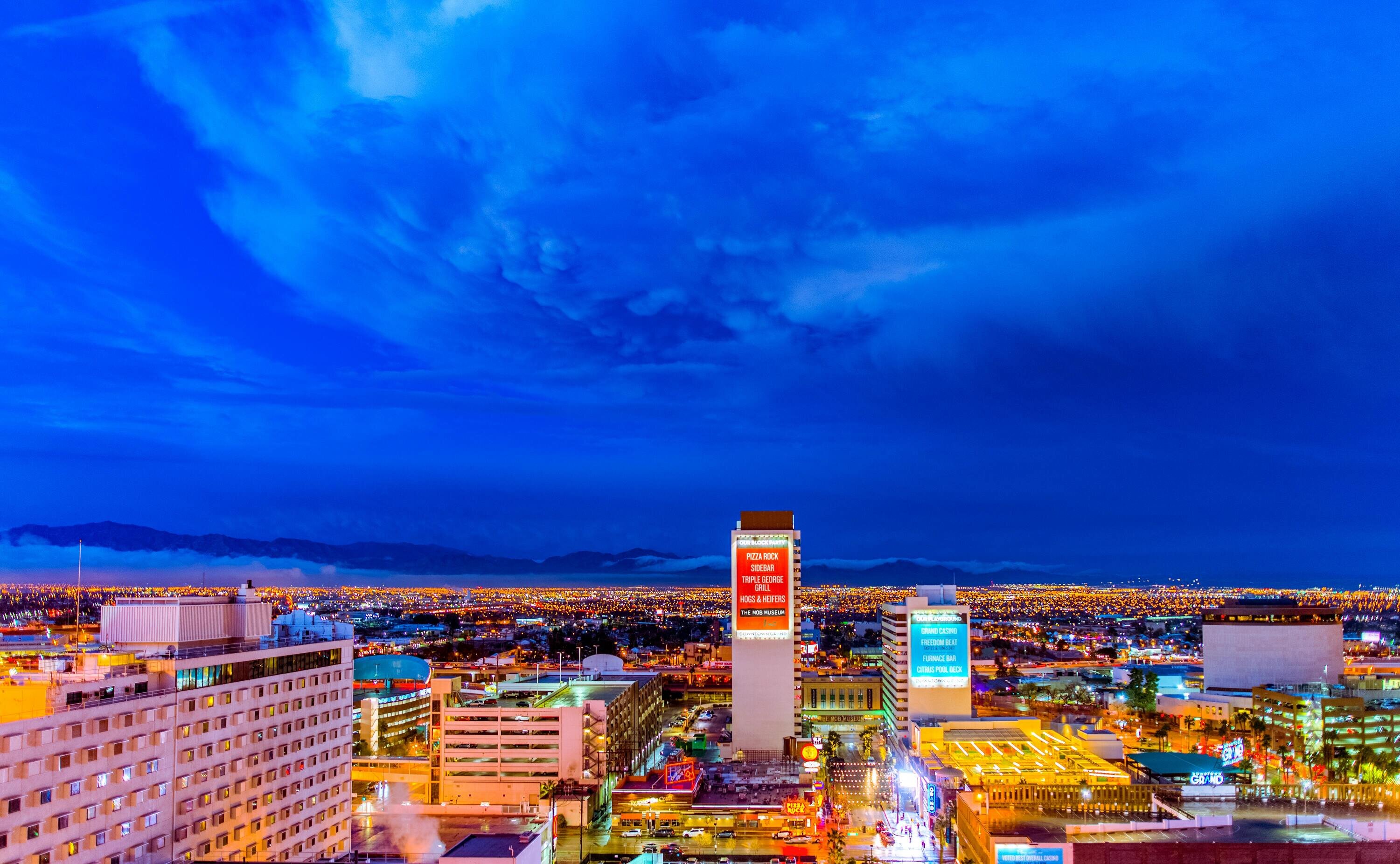 A vibrant cityscape at night with brightly lit buildings, colorful lights, and a deep blue sky stretching over the horizon.