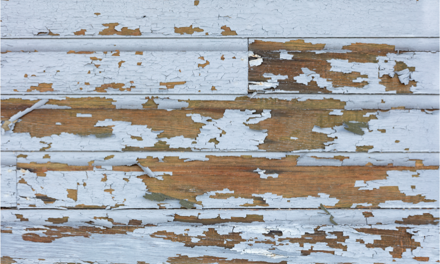 Close-up photo of weathered wooden siding with peeling white paint, revealing underlying wood, indicative of potential lead paint issues in older homes.