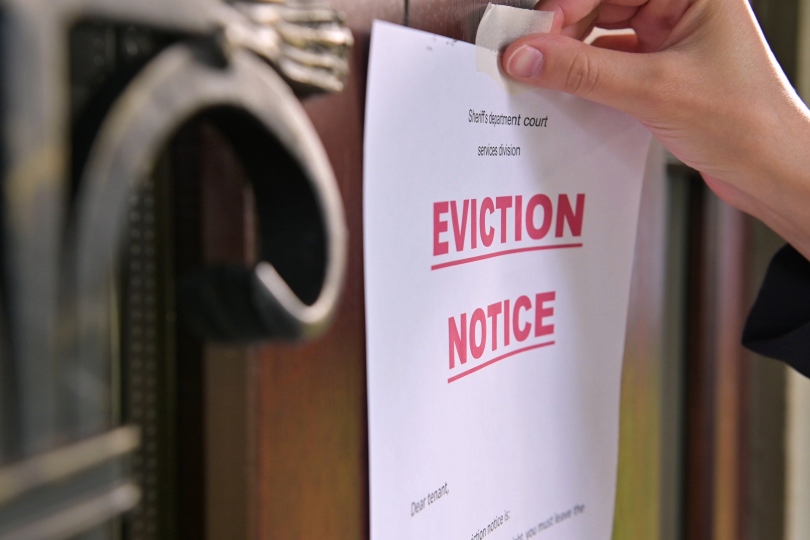 A close-up view of a person's hand affixing an 'Eviction Notice' to a door, indicating the start of the eviction process for a tenant in Ohio.